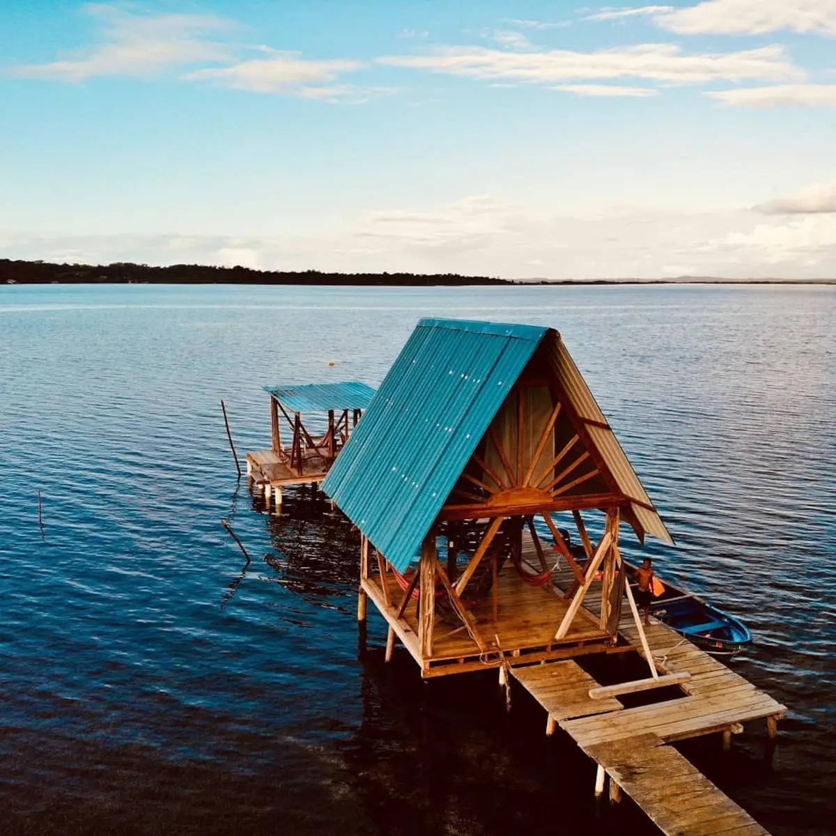 Teal-roofed cabin on stilts over a calm bay